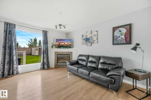 Spacious living area featuring wood-finish flooring, a contemporary fireplace with a tiled surround and mantel, and a large window overlooking the backyard - 2921 23 Street, Edmonton, AB 