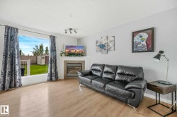 Spacious living area featuring wood-finish flooring, a contemporary fireplace with a tiled surround and mantel, and a large window overlooking the backyard - 