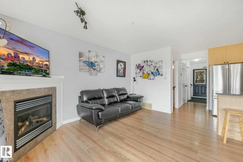 Living area featuring wood-finish flooring, a corner fireplace with a tile surround and mantel, vaulted ceilings, and track lighting - 2921 23 Street, Edmonton, AB 