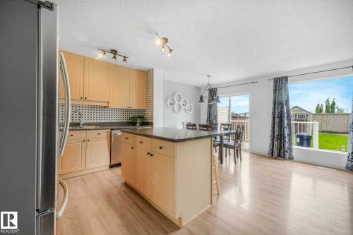 Kitchen featuring light wood cabinetry, a central island with a dark countertop, stainless steel appliances, and wood-finish flooring - 2921 23 Street, Edmonton, AB 