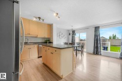 Kitchen featuring light wood cabinetry, a central island with a dark countertop, stainless steel appliances, and wood-finish flooring - 