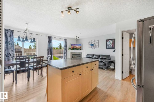 Open-concept living space featuring wood-finish flooring, a kitchen island with stone-finish countertop, and a dining area with a contemporary chandelier - 2921 23 Street, Edmonton, AB 