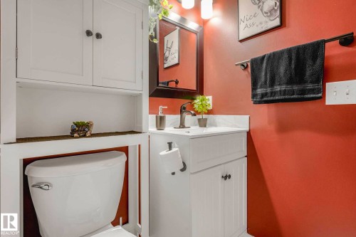 Bathroom featuring a single vanity with a white countertop and integrated sink, a dark bronze faucet, and a wall-mounted mirror - 2921 23 Street, Edmonton, AB 