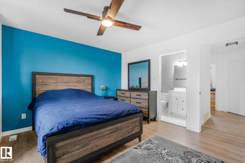 Spacious room featuring light wood-finish flooring, a ceiling fan with integrated lighting, and a vibrant accent wall - 2921 23 Street, Edmonton, AB 