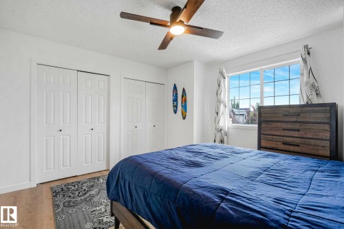 Bedroom featuring light wood-finish flooring, a ceiling fan with integrated lighting, white bi-fold closet doors, and a large window - 2921 23 Street, Edmonton, AB 