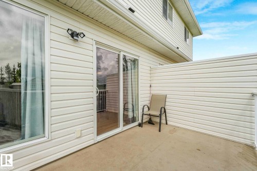 Private outdoor patio space featuring durable concrete flooring, white vinyl siding, and an exterior wall fixture with floodlights - 2921 23 Street, Edmonton, AB 