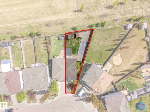 Property outlined by red boundary line, featuring a residential structure with a brown shingle roof, two detached storage sheds, and a substantial grass lawn - 2921 23 Street, Edmonton, AB 