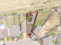 Property outlined by red boundary line, featuring a residential structure with a brown shingle roof, two detached storage sheds, and a substantial grass lawn - 