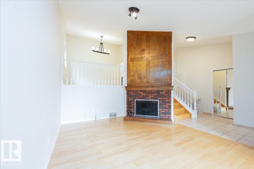 Living area featuring a brick fireplace with a wood mantle, light wood-finish flooring, and an open staircase with white railings - 4107 147 Street, Edmonton, AB 