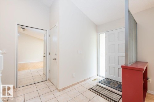 Entryway featuring light-toned tile flooring, a paneled front door with a sidelight, and a vaulted ceiling - 4107 147 Street, Edmonton, AB 
