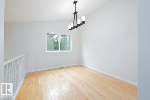 Bright room featuring wood-finish flooring, a white spindle railing, and a contemporary linear chandelier with frosted glass shades - 4107 147 Street, Edmonton, AB 