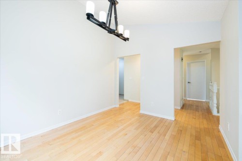 Spacious interior featuring wood-finish flooring, a contemporary black metal chandelier with four white cylindrical lights, and light-toned walls - 4107 147 Street, Edmonton, AB 