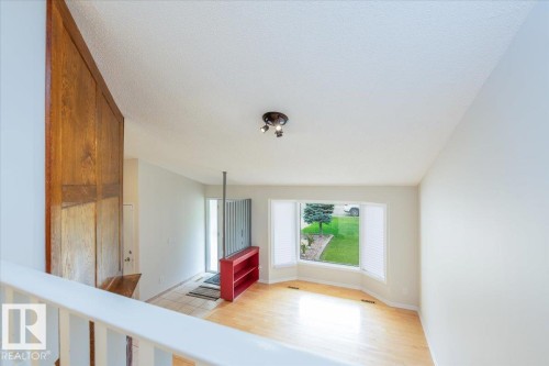 Bright living area featuring wood-finish flooring, a bay window with white blinds, and a neutral wall color - 4107 147 Street, Edmonton, AB 