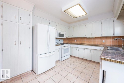 Kitchen featuring extensive white cabinetry, tile flooring, brown subway tile backsplash, laminate countertops, and a dual basin stainless steel sink - 4107 147 Street, Edmonton, AB 