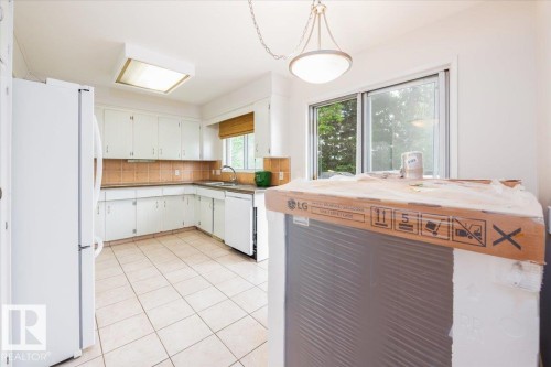 Kitchen featuring white cabinetry, tile flooring, tile backsplash, and a sliding glass door - 4107 147 Street, Edmonton, AB 