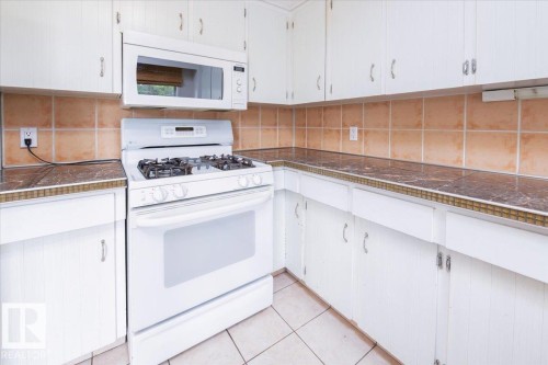 Corner kitchen featuring white cabinetry, a white gas range with an overhead microwave, and a tiled backsplash - 4107 147 Street, Edmonton, AB 
