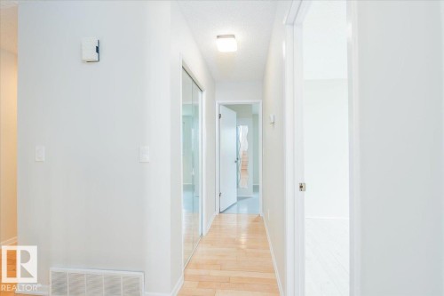 Hallway featuring wood-finish flooring, white walls, and a ceiling-mounted light fixture - 4107 147 Street, Edmonton, AB 