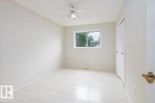 Bright interior space featuring a window, wood-finish flooring, a ceiling fan with integrated lighting, and a white bi-fold closet door with dark hardware - 4107 147 Street, Edmonton, AB 