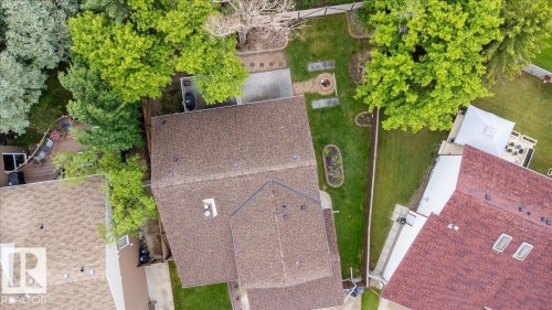 Expansive backyard featuring a manicured lawn, established trees, concrete patio, and a fire pit - 4107 147 Street, Edmonton, AB 