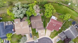 Aerial perspective showcasing a residential property with a brown shingle roof, a concrete driveway, and a spacious green lawn - 