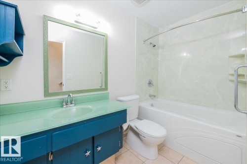 Bathroom featuring a glass countertop vanity with an integrated basin, a framed mirror, and a tub-shower combination with a textured surround - 4107 147 Street, Edmonton, AB 