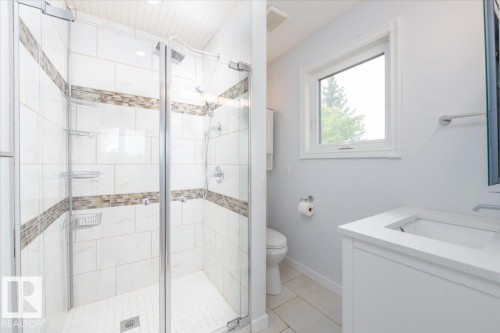 Glass-enclosed shower with white tiled walls, decorative accent tile bands, and a built-in shower head - 4107 147 Street, Edmonton, AB 