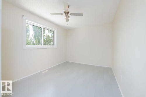 Bright room featuring light wood-finish flooring, a white ceiling fan with integrated lighting, and a large window with white framing - 4107 147 Street, Edmonton, AB 