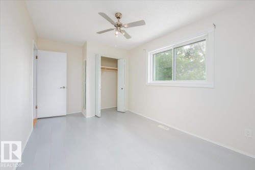 Room featuring light-toned walls, a window with exterior tree views, a ceiling fan with integrated lighting, and a closet with bifold doors - 4107 147 Street, Edmonton, AB 