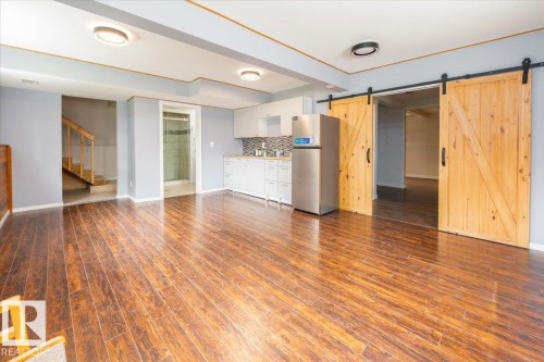 Spacious room featuring wood-finish flooring, a kitchen area with white cabinetry and a mosaic tile backsplash, and two wood barn doors - 4107 147 Street, Edmonton, AB 