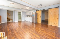 Spacious room featuring wood-finish flooring, a kitchen area with white cabinetry and a mosaic tile backsplash, and two wood barn doors - 