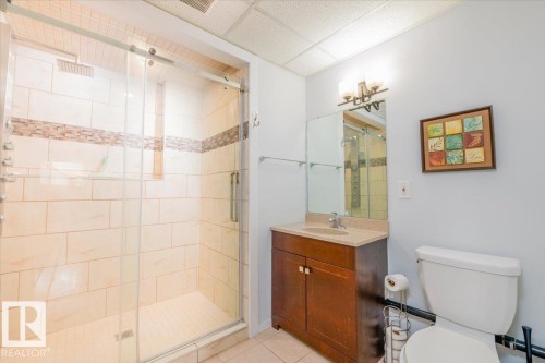 Shower enclosure featuring a glass sliding door, light-toned tile surround with a decorative accent band, and a built-in shower niche - 4107 147 Street, Edmonton, AB 