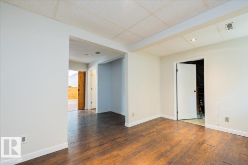 Spacious room featuring rich wood-finish flooring, white walls, and a dropped acoustic panel ceiling with recessed lighting - 4107 147 Street, Edmonton, AB 