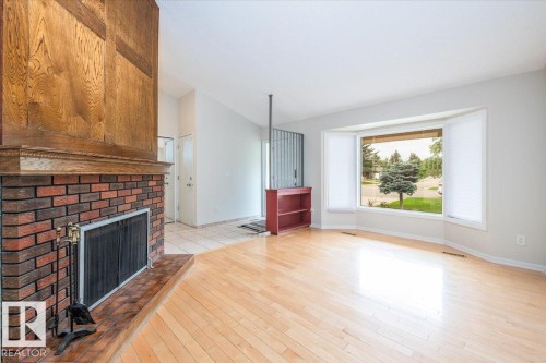 Living area featuring wood-finish flooring, a brick fireplace with a wood mantle and surround, a prominent bay window, and a built-in shelving unit - 4107 147 Street, Edmonton, AB 