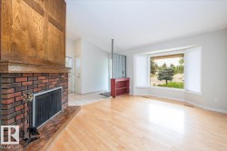 Living area featuring wood-finish flooring, a brick fireplace with a wood mantle and surround, a prominent bay window, and a built-in shelving unit - 