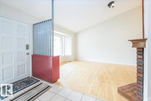 Entryway featuring a panel door with a smart lock, leading to a living area with wood-finish flooring, a vaulted ceiling, and a brick fireplace with a decorative wood mantel - 4107 147 Street, Edmonton, AB 