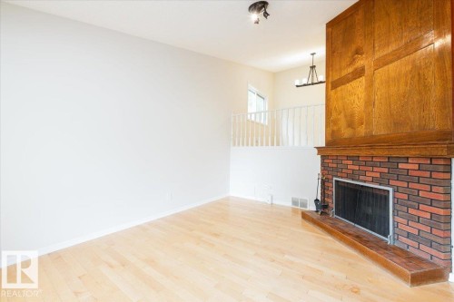 Living area featuring light wood-finish flooring, white walls, and a brick fireplace with a wood mantle and surround - 4107 147 Street, Edmonton, AB 