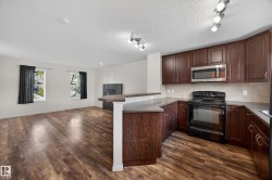 Open-concept living space featuring wood-finish flooring, a corner fireplace with stone surround, two windows with dark curtains, dark wood cabinetry, and a black range with an over-the-range microwave - 
