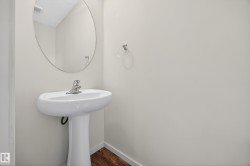Pedestal sink with chrome faucet, complemented by an oval wall mirror and wood-finish flooring - 