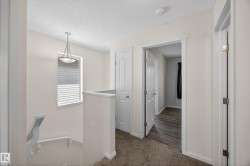 Upper-level hallway featuring neutral wall tones, textured ceiling, and a prominent window with horizontal blinds - 