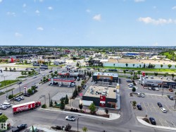 Aerial perspective showcasing a commercial development with multiple single-story retail buildings, extensive surface parking, and a gas station - 