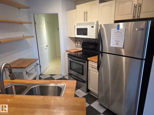Kitchen featuring wood-finish countertops, a double basin stainless steel sink, and a pull-down faucet - 35 10331 106 Street, Edmonton, AB 