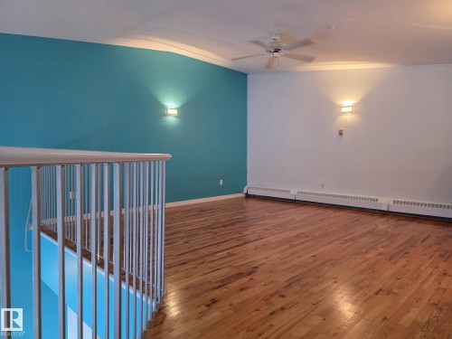Open concept upper level featuring wood-finish flooring, a ceiling fan, and wall-mounted sconces - 35 10331 106 Street, Edmonton, AB 