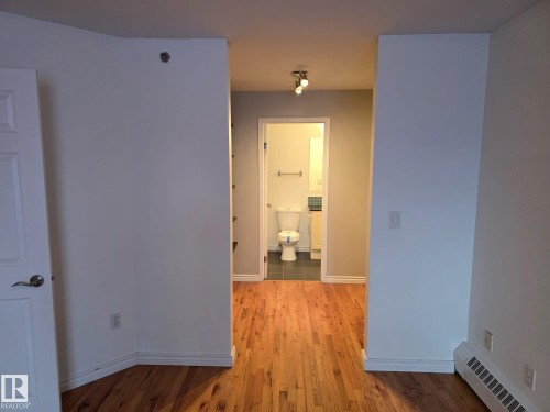 Wood-finish flooring extending from the foreground into the background, showcasing a white interior door with a silver handle - 35 10331 106 Street, Edmonton, AB 