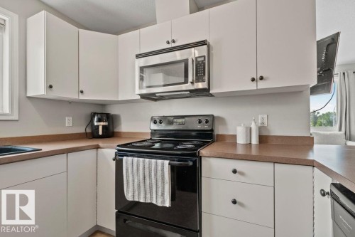 Kitchen featuring white cabinetry, a stainless steel over-the-range microwave, a black electric range, and laminate countertops - 232 4309 33 Street, Stony Plain, AB 