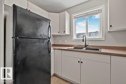 Kitchen featuring white cabinetry, a double basin sink with a matte black faucet, and a large window - 232 4309 33 Street, Stony Plain, AB 