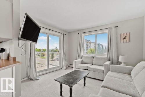Bright open-concept living area featuring light-toned walls, neutral carpeting, and a sliding glass door providing outdoor access - 232 4309 33 Street, Stony Plain, AB 