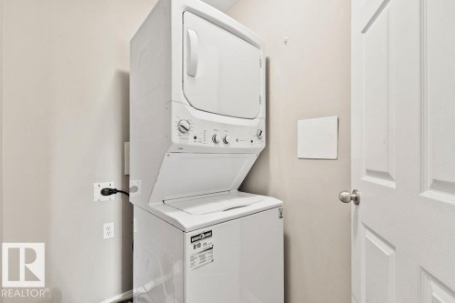 Laundry area featuring a white stacked washer and dryer, light neutral wall paint, and a white paneled door with a brushed nickel knob - 232 4309 33 Street, Stony Plain, AB 