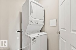 Laundry area featuring a white stacked washer and dryer, light neutral wall paint, and a white paneled door with a brushed nickel knob - 