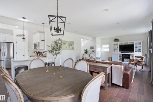 Open-concept interior featuring wood-finish flooring, white cabinetry, stainless steel appliances, a kitchen island with seating, and a built-in entertainment center with a fireplace - 34 Falcon Road, Cold Lake, AB 