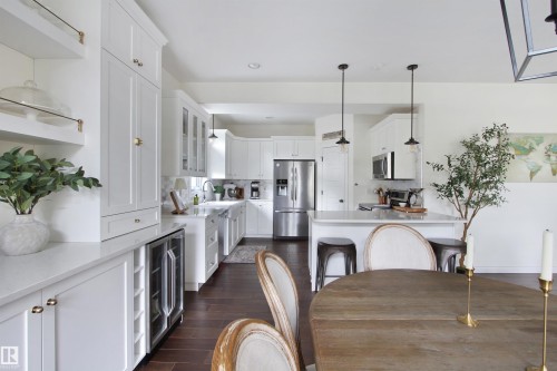 Kitchen featuring white shaker-style cabinetry, stainless steel appliances, a built-in beverage refrigerator, a central island with counter seating, and dark wood-finish flooring - 34 Falcon Road, Cold Lake, AB 